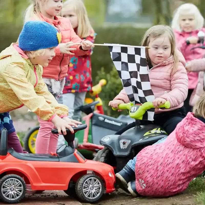 Kindergartenkinder mit und ohne Behinderung machen ein Rutschauto Rennen.