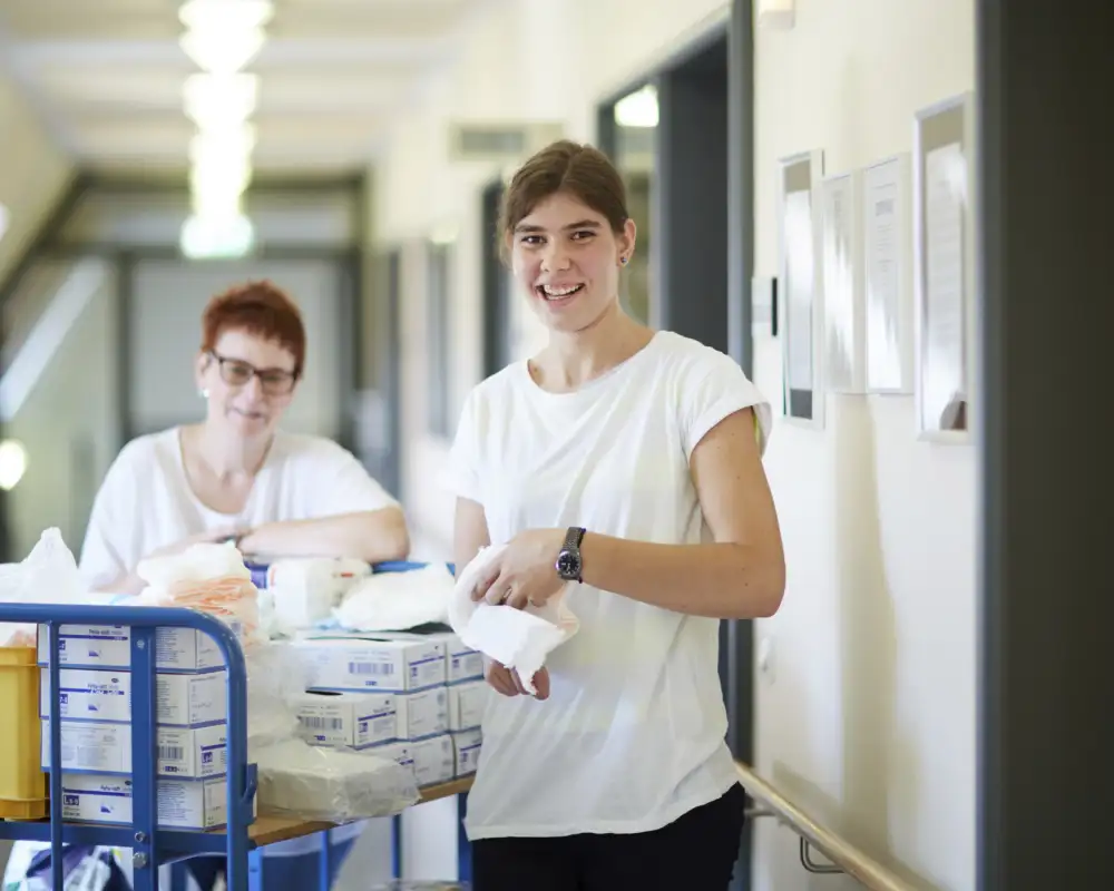 Zwei Frauen stehen in einem Korridor mit einem Material-Wagen.