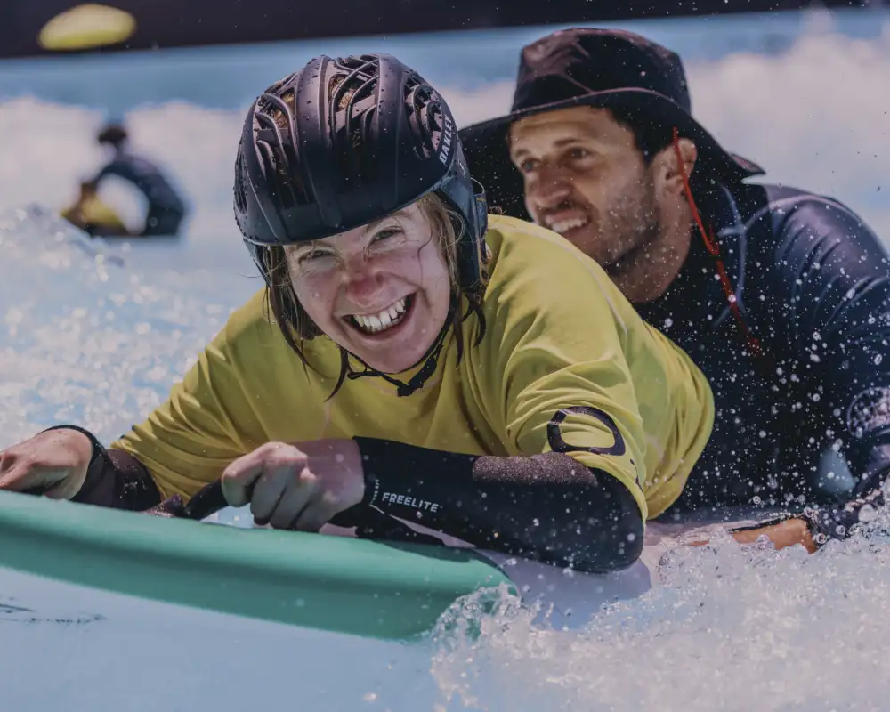Zwei Personen in Neoprenanzügen liegen auf einem Surfbrett.