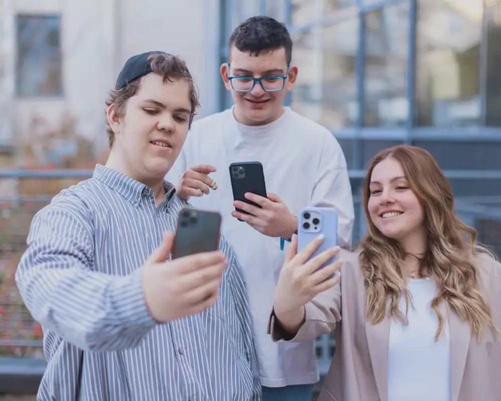 Drei Jugendliche stehen nebeneinander und machen Selfies mit ihren Handys.