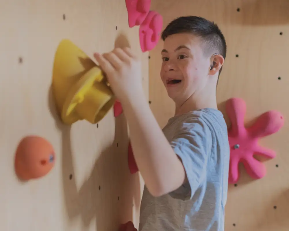 Ein junger Mann mit Down-Syndrom klettert an einer Boulderwand.
