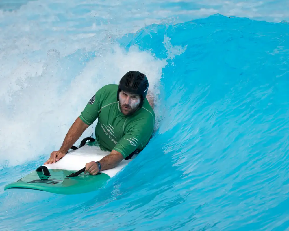 Ein Mann liegt auf einem Surfbrett und gleitet damit durch eine Welle.