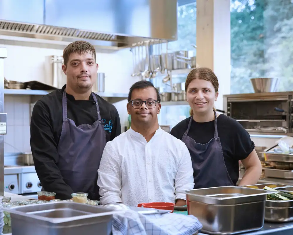 Drei junge Erwachsene unterschiedlicher Herkunft stehen in einer Café-Küche.