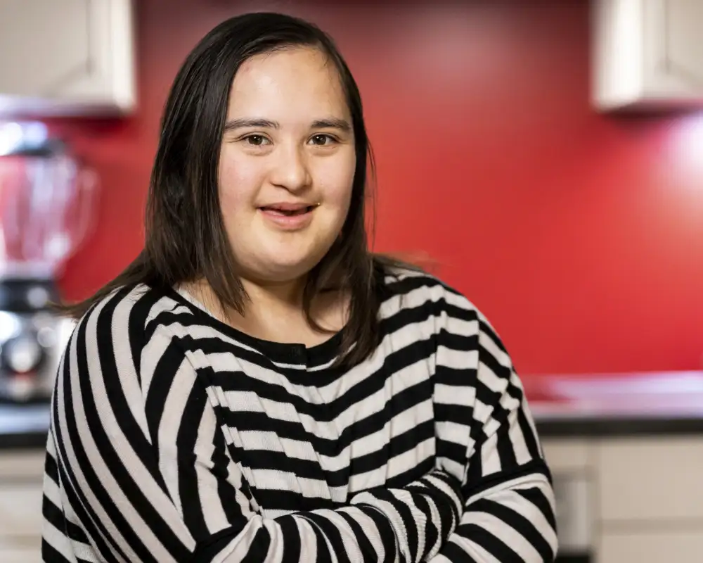 Eine junge Frau mit Down-Syndrom lächelt in die Kamera.