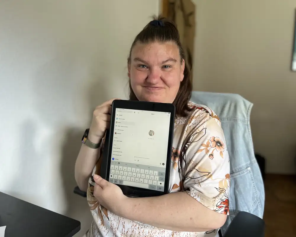 Eine junge Frau hält ein Tablet in den Armen und lächelt in die Kamera.