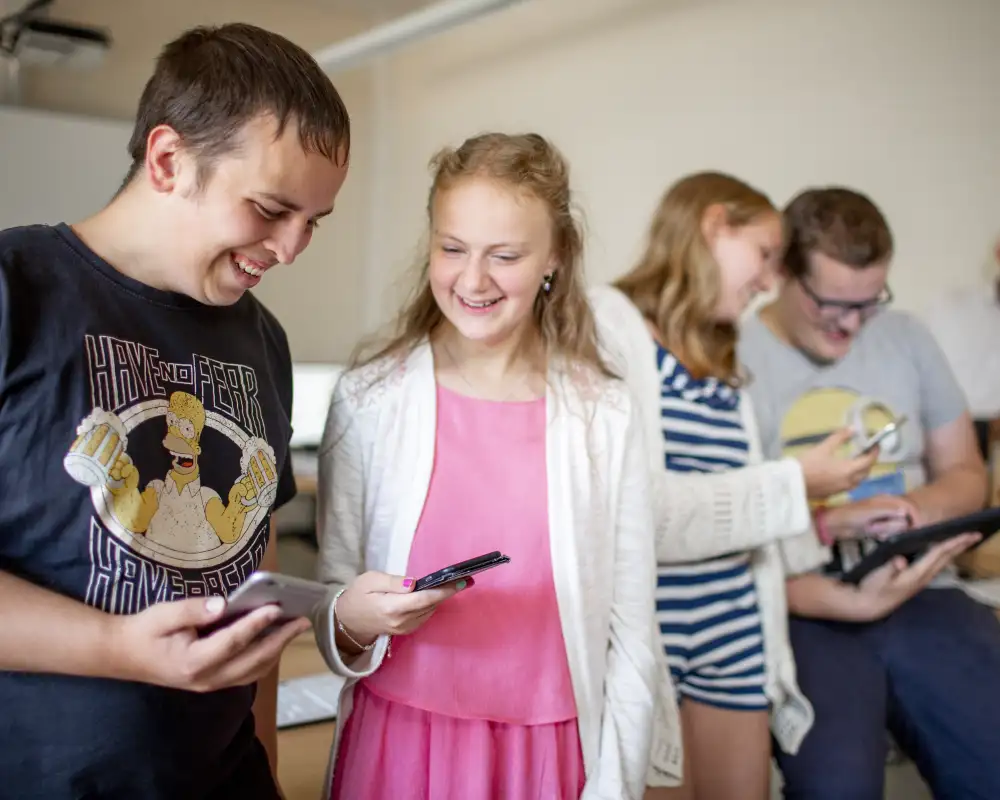 Zwei Jugendliche stehen nebeneinander und schauen lachend auf ihre Smartphones.