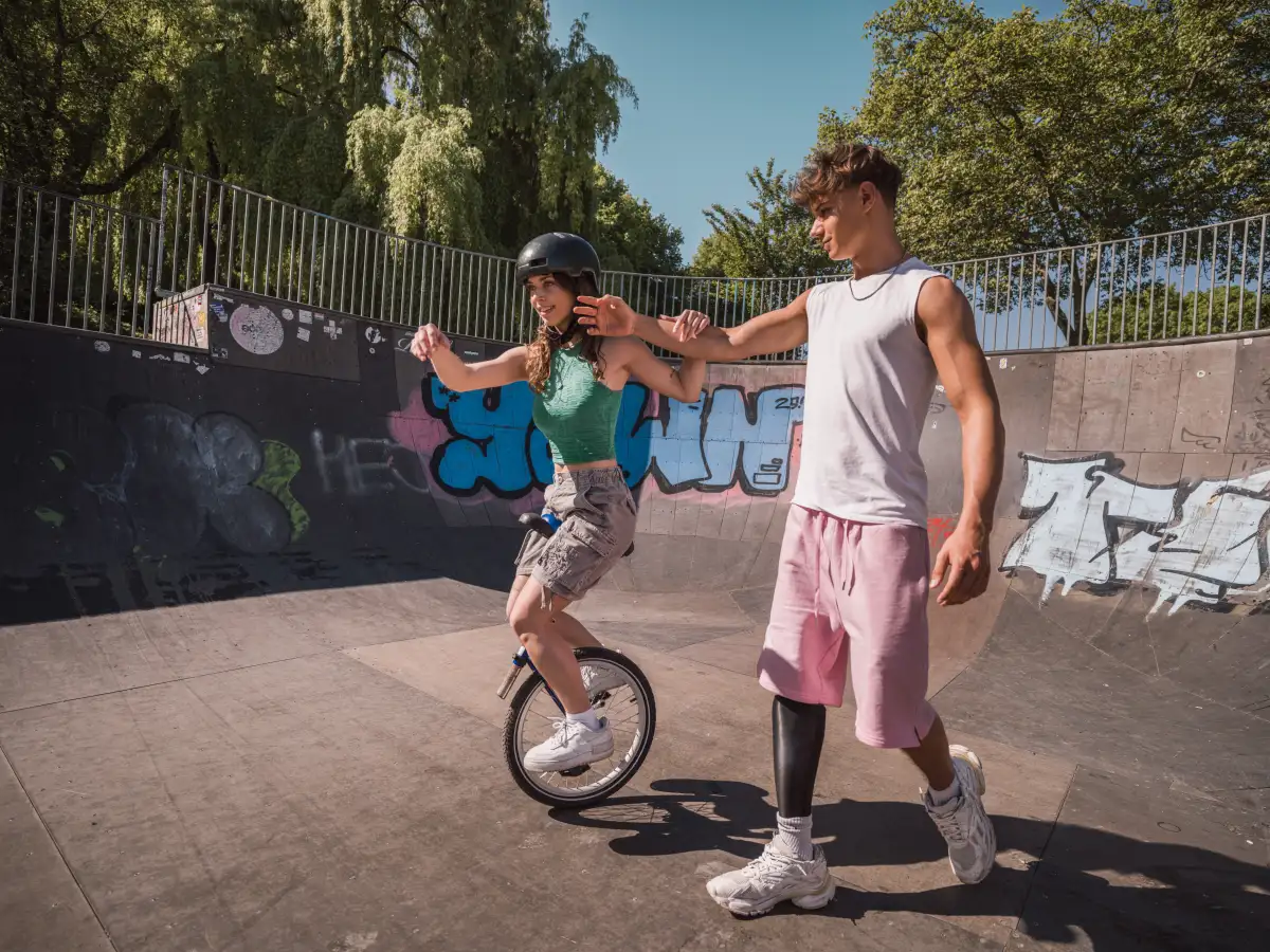 Eine Jugendliche sitzt auf einem Einrad. Sie wird von einem anderen Jugendlichen gestützt.
