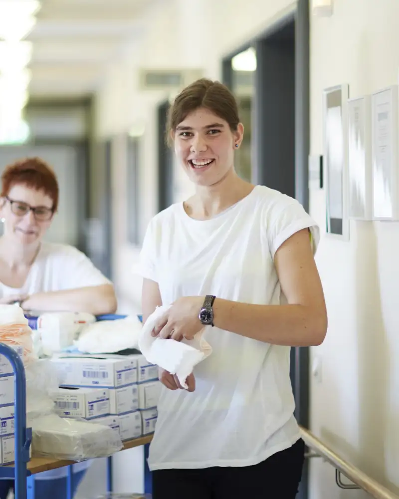 Zwei Frauen stehen in einem Korridor mit einem Material-Wagen.