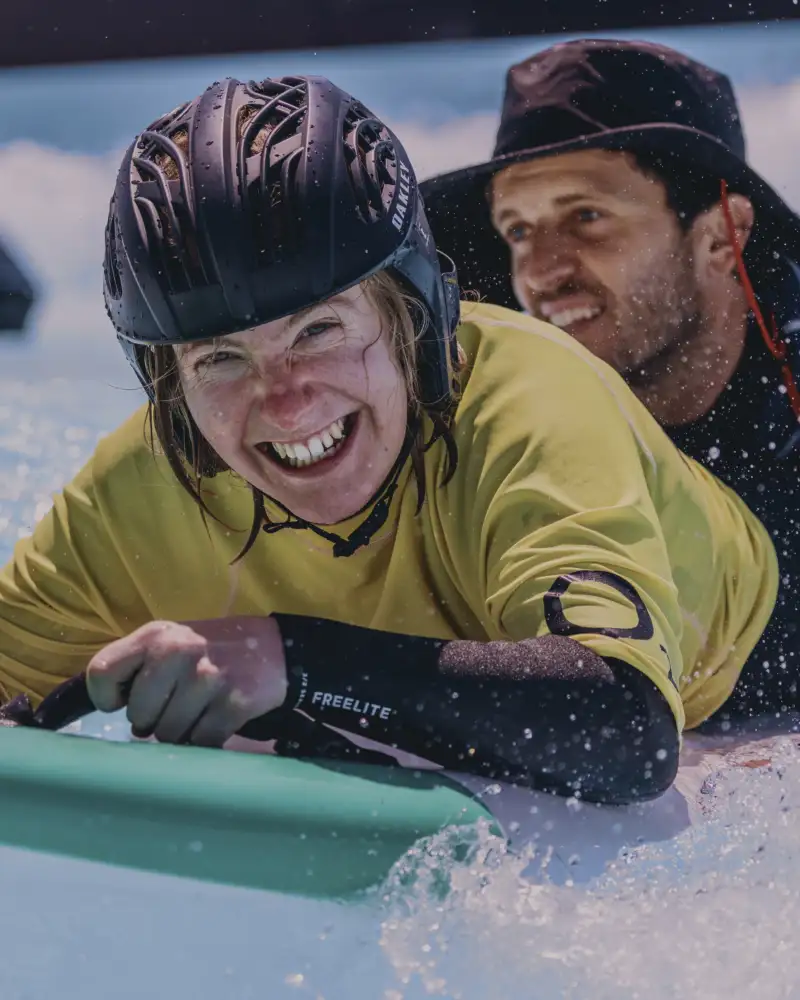 Zwei Personen in Neoprenanzügen liegen auf einem Surfbrett.