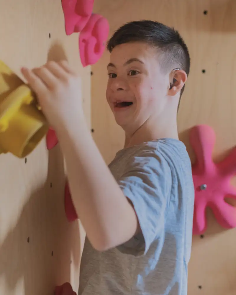 Ein junger Mann mit Down-Syndrom klettert an einer Boulderwand.