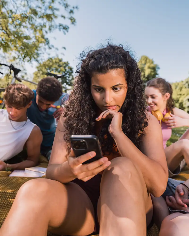 Jugendliche sitzen auf einer Wiese und schauen in ihre Smartphones.
