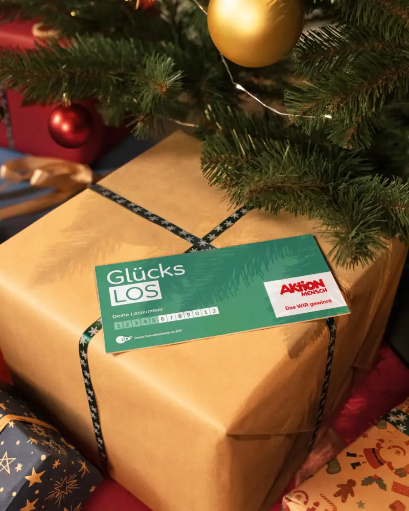 Ein Aktion Mensch-Glücks-Los liegt auf einem Weihnachtsgeschenk.