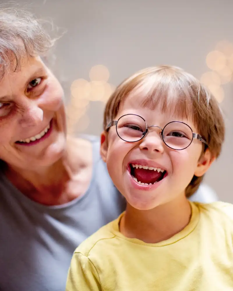 Eine Frau und ein Kind mit Down-Syndrom. Beide lachen in die Kamera.