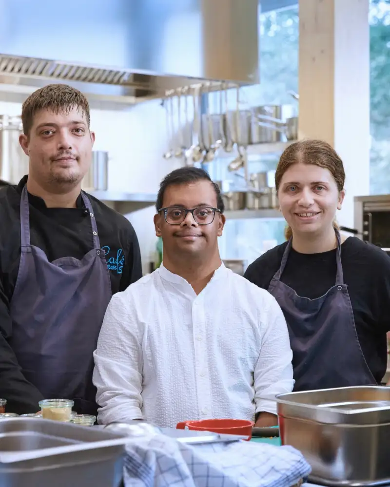 Drei junge Erwachsene unterschiedlicher Herkunft stehen in einer Café-Küche.
