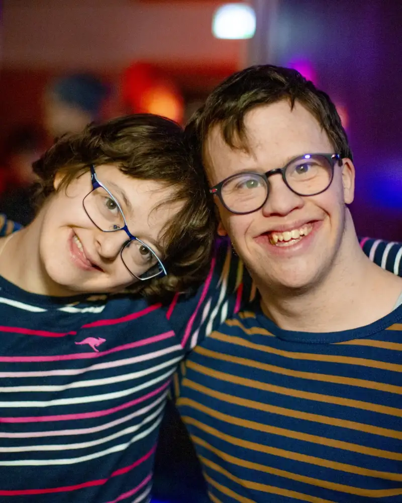 Zwei junge Menschen liegen sich in den Armen und lächeln in die Kamera.