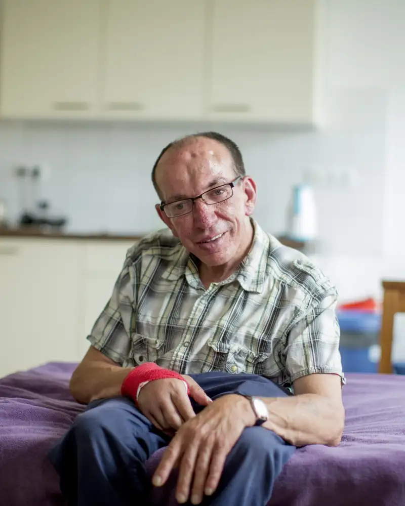 Ein Mann mit geistiger Behinderung sitzt in seinem Appartement auf seinem Bett.