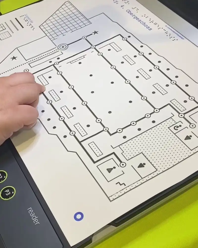 Eine Hand folgt mit dem Finger den Linien eines taktilen Lageplans.
