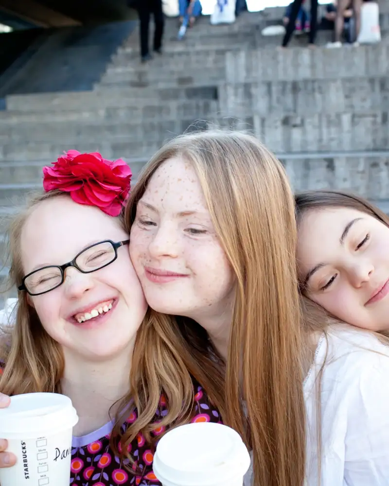 Drei Mädchen stehen vor einer Treppe und umarmen sich.