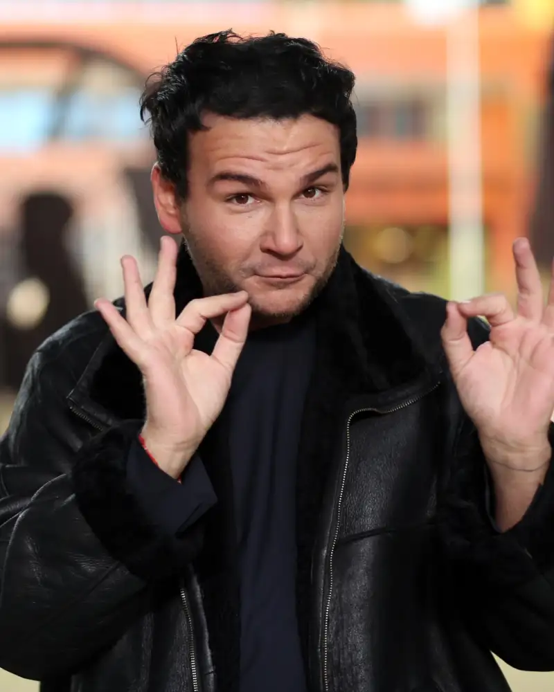 Ein junger Mann mit dunklen Haaren und Lederjacke macht mit seinen Händen eine Gebärde der Deutschen Gebärdensprache.