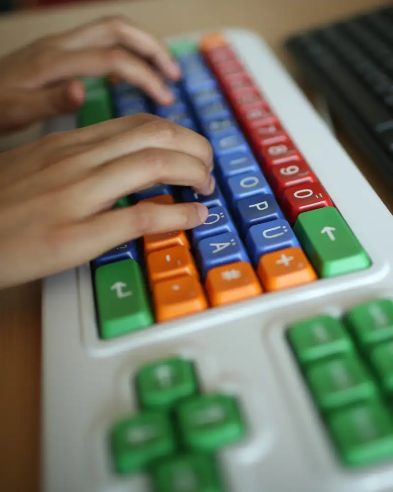 Zwei Hände auf einer bunten Tastatur.