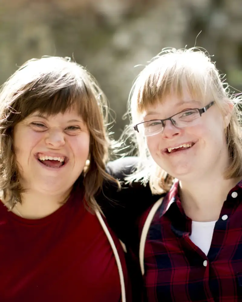 Zwei junge Frauen umarmen sich und lachen in die Kamera.