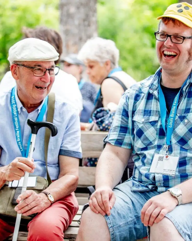 Ein junger und ein alter Mann sitzen auf einer Bank und lachen gemeinsam.