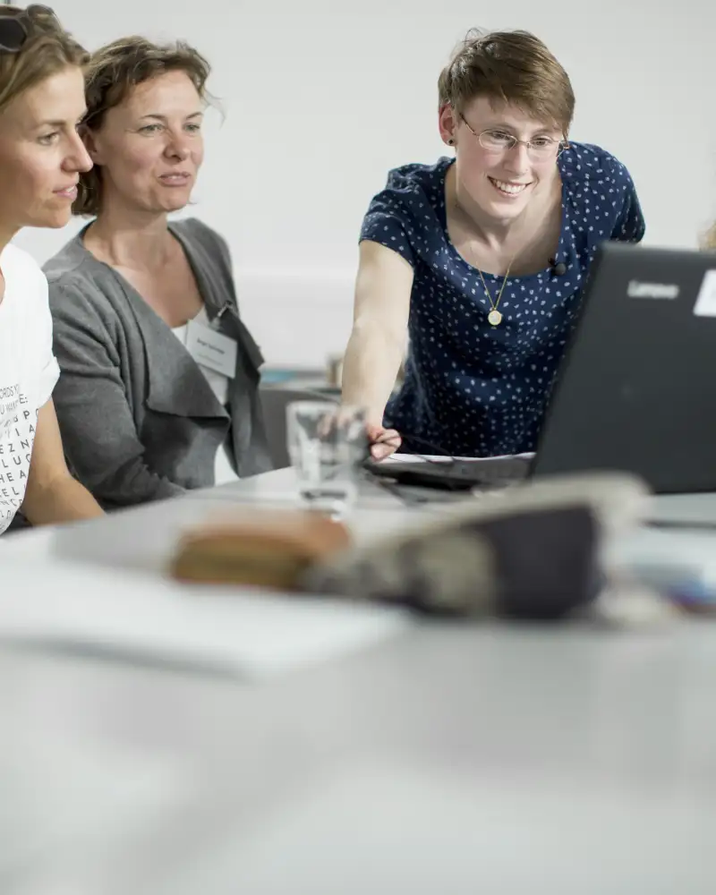 Vier Frauen und ein Mann sitzen an einem Konferenztisch und schauen gemeinsam auf einen Laptop-Monitor.