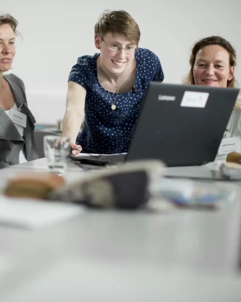Vier Frauen und ein Mann sitzen an einem Konferenztisch und schauen gemeinsam auf einen Laptop-Monitor.
