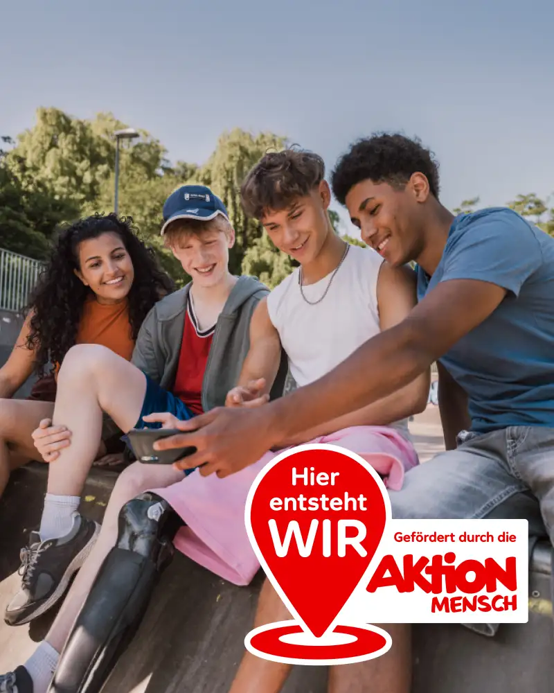 Vier Jugendliche mit und ohne Behinderung sitzen in sommerlicher Kleidung nebeneinander auf einer Mauer. Sie schauen gut gelaunt gemeinsam auf ein Smartphone. Im Vordergrund sieht man den Aktionsstempel zu #HierEntstehtWIR: Ein Standorticon mit der Aufschrift "Hier entsteht WIR" und daneben der Text "Gefördert durch die Aktion Mensch".
