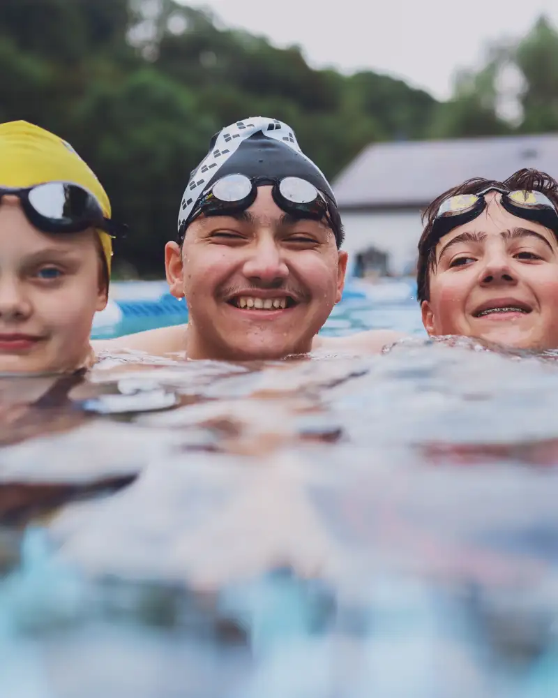 Zwei Jungen und ein Mädchen schwimmen im Schwimmbecken.