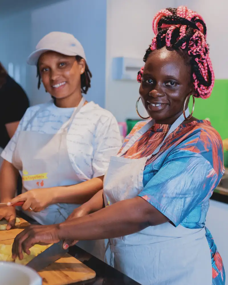 Zwei junge Frauen stehen in einer Küche und schneiden Kartoffeln in kleine Würfel.