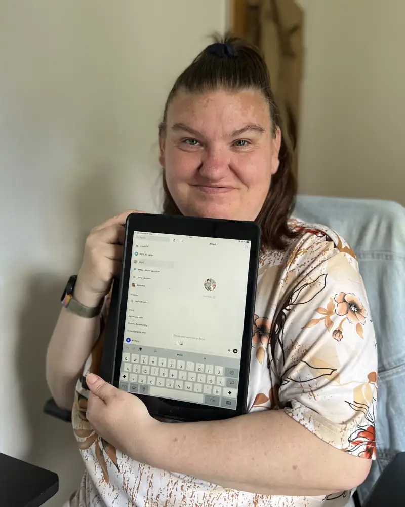 Eine junge Frau hält ein Tablet in den Armen und lächelt in die Kamera.