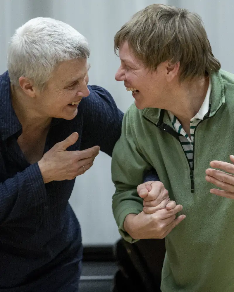 Zwei ältere Frauen stehen Arm in Arm nebeneinander und lachen sich an.