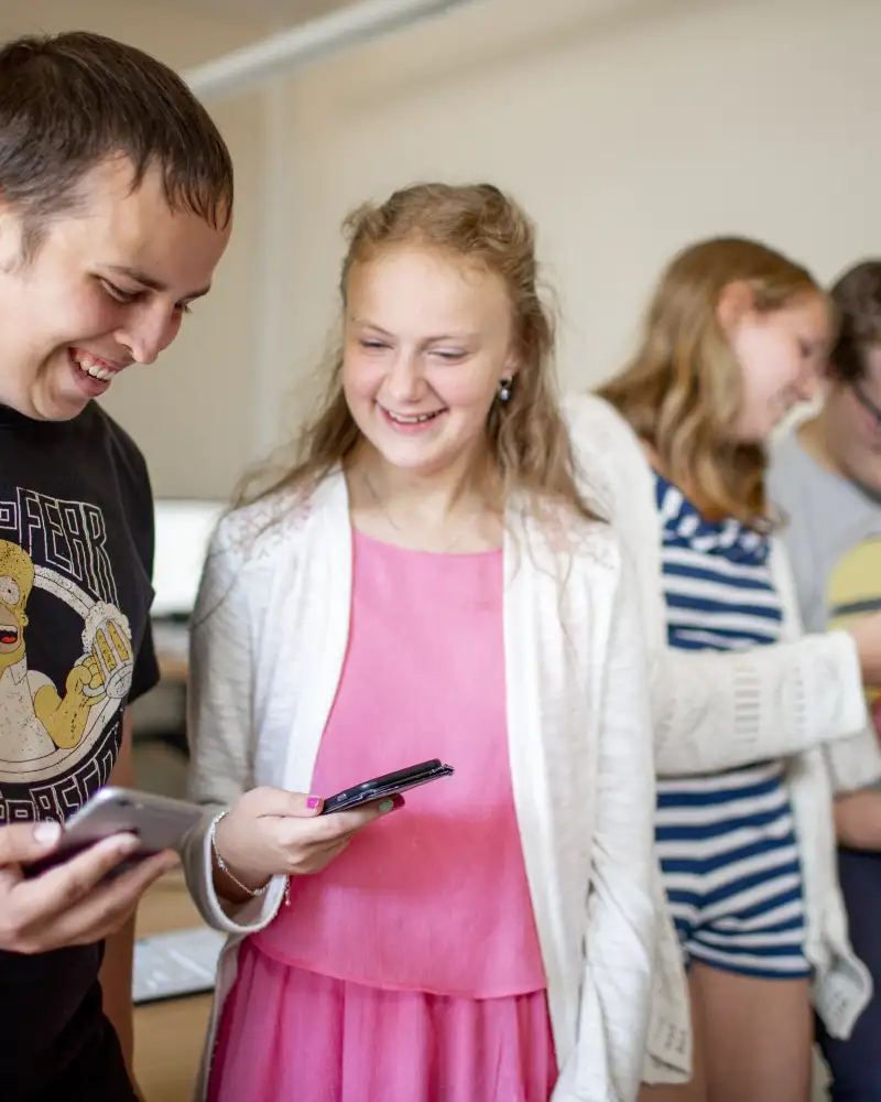 Zwei Jugendliche stehen nebeneinander und schauen lachend auf ihre Smartphones.