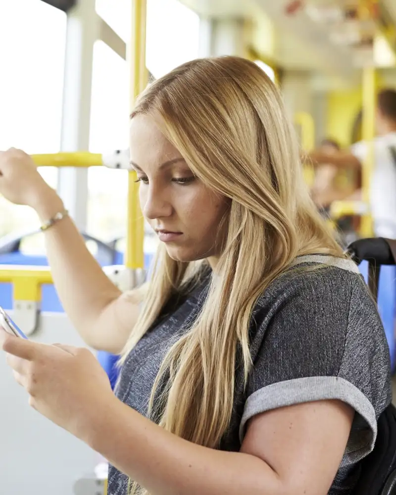 Eine Jugendlich im Rollstuhl befindet sich im Bus und schaut auf ihr Smartphone.