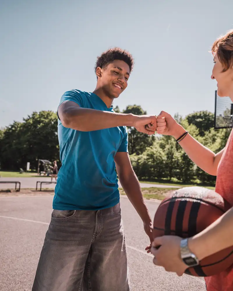 Zwei Jugendliche auf einem Basketballplatz klatzschen sich ab.