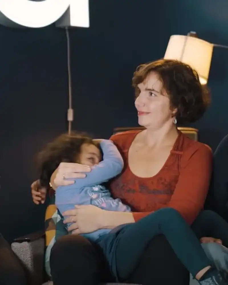 Drei blinde Menschen sitzen nebeneinander und schauen sich an. In der Mitte sitzt eine Frau, die ein vierjähriges Kind auf dem Schoß hat.