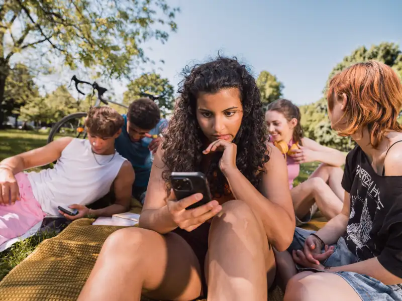 Jugendliche sitzen auf einer Wiese und schauen in ihre Smartphones.
