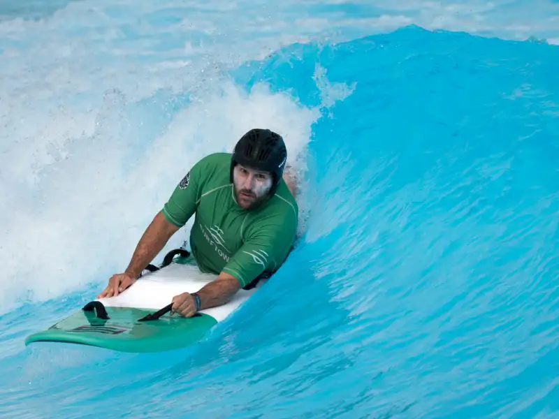 Ein Mann liegt auf einem Surfbrett und gleitet damit durch eine Welle.