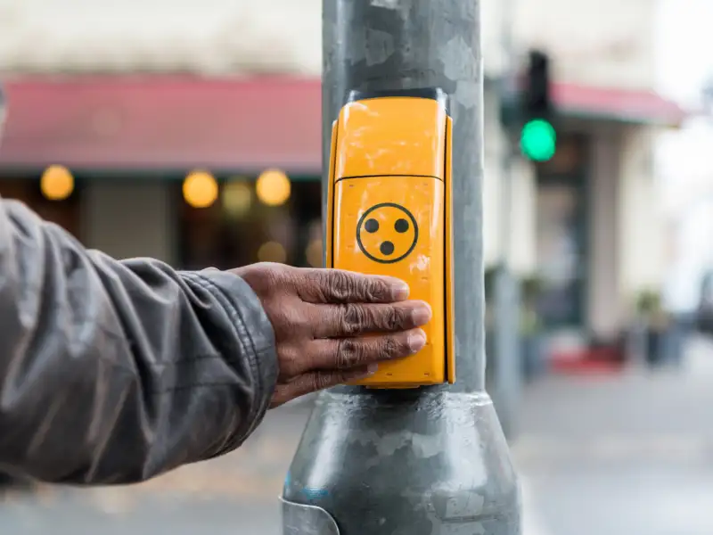 Eine Hand liegt auf einem Ampel-Anforderungstaster.