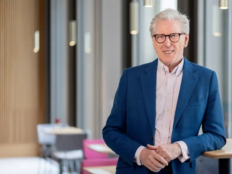 Grauhaariger Mann Mitte sechzig mit Brille in blauer Anzugsjacke