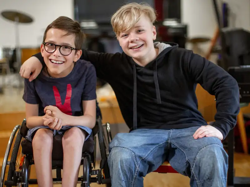 Zwei Jungen, einer davon im Rollstuhl, lachen gemeinsam.