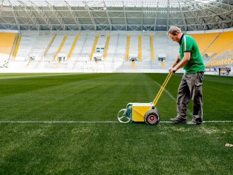 Ein Mann pflegt den Rasen in einem Fußballstadion.