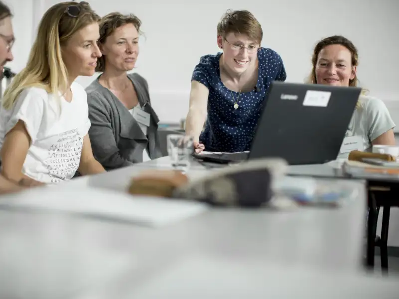 Vier Frauen und ein Mann sitzen an einem Konferenztisch und schauen gemeinsam auf einen Laptop-Monitor.