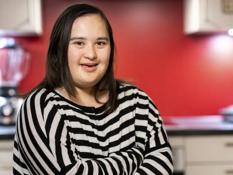Eine junge Frau mit Down-Syndrom lächelt in die Kamera.
