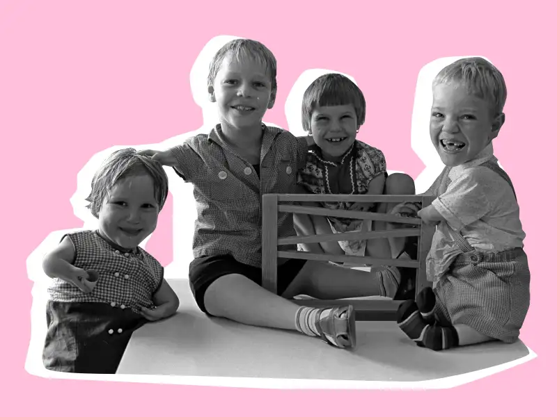 Schwarz-weiß-Aufnahme aus den 60ern: Vier Kinder mit Köperbehinderungen sitzen auf einem Tisch und spielen mit einer Murmelbahn. Sie lachen.