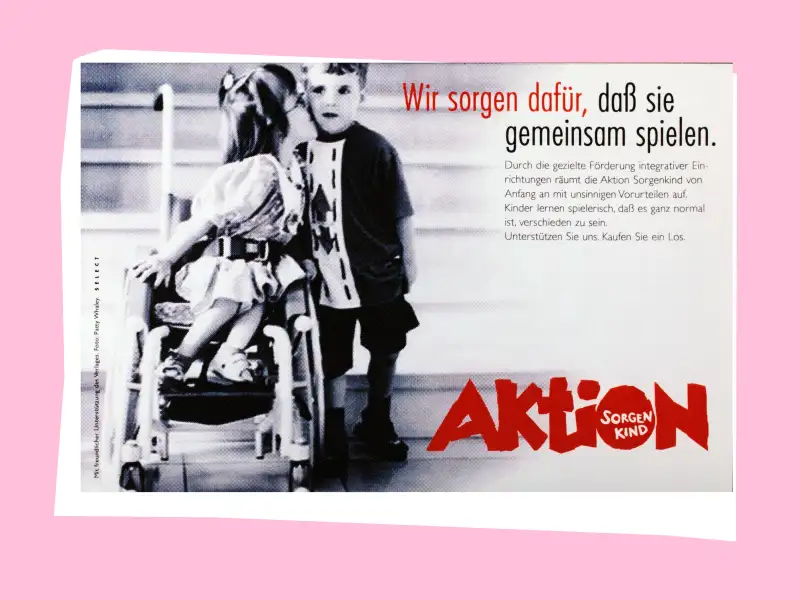 in Mädchen im Rollstuhl küsst einen Jungen neben ihr auf die Wange. Rechts steht der Schriftzug "Wir sorgen dafür, dass sie gemeinsam spielen".