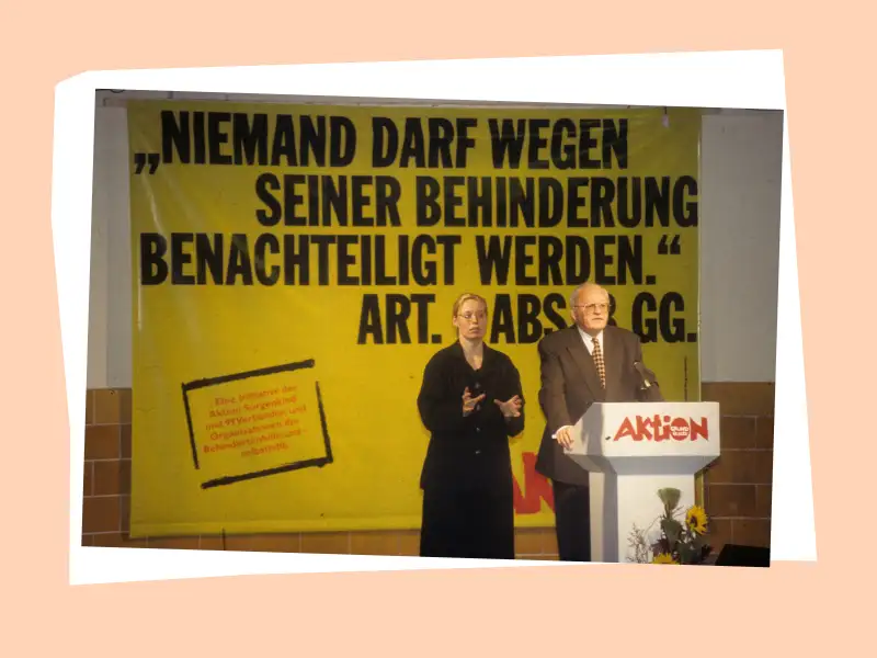 Roman Herzog steht auf einem Podium. Neben ihm steht eine Gebärdensprachdolmetscherin. Im Hintergrund ist ein Plakat mit der Aufschrift "Niemand darf wegen seiner Behinderung benachteiligt werden." zu sehen.