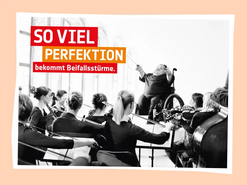 Benedikt Lika sitzt im Rollstuhl und dirigiert ein Orchester. Oben rechts steht der Schriftzug "So viel Perfektion bekommt Beifallsstürme".