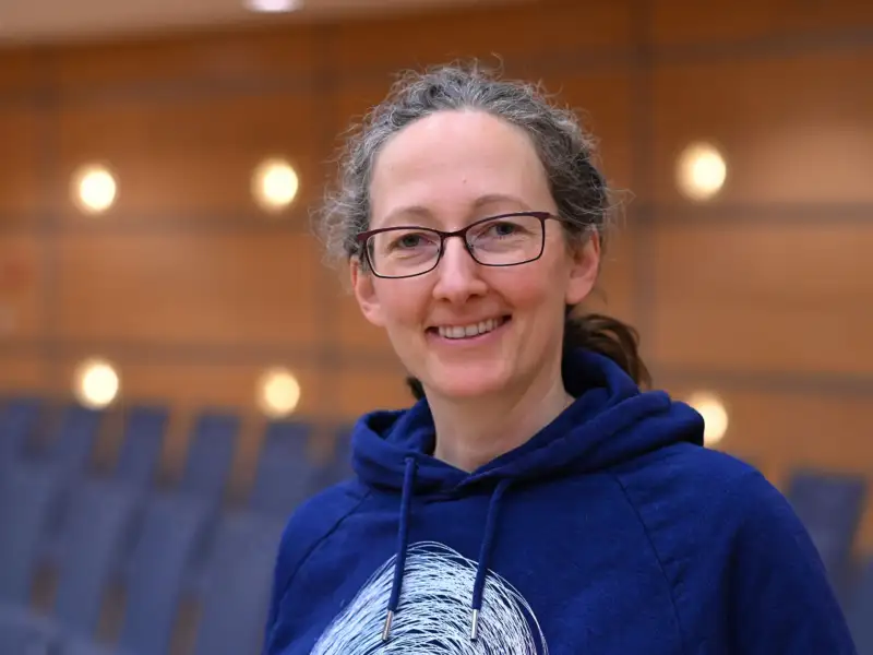 Porträtfoto von Conny Lopez. Sie trägt Brille, einen blauen Kapuzenpulli und einen Pferdeschwanz und lächelt in die Kamera.
